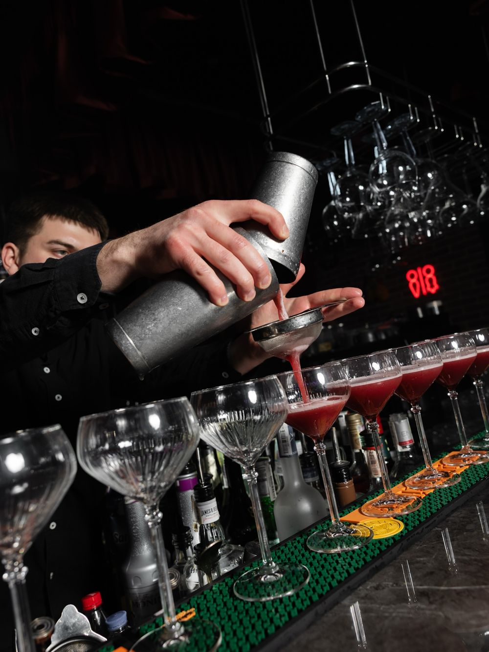 Бармен розливає коктейль у ряд келихів за стійкою
